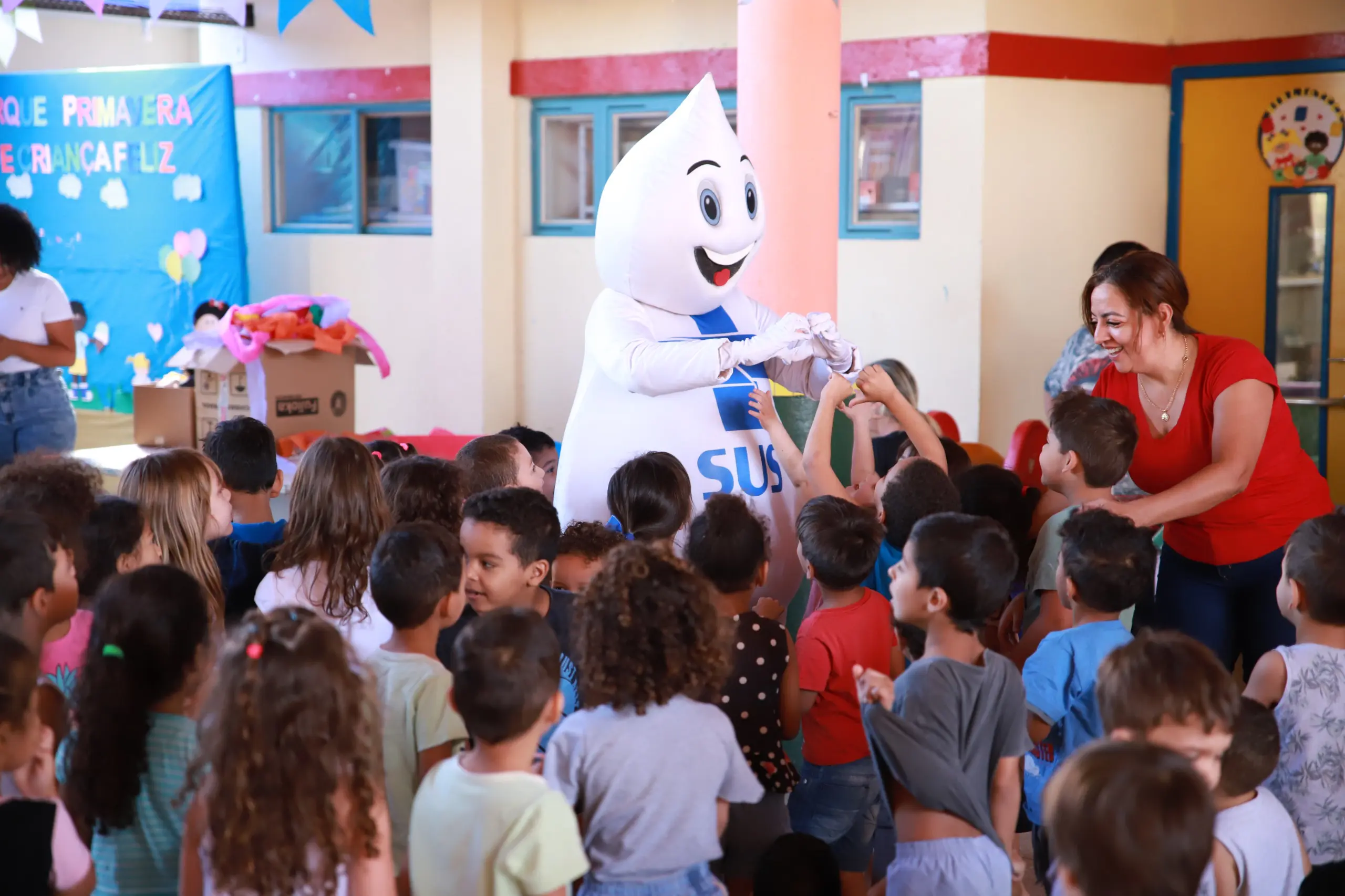 Foto do Zé Gotinha com várias crianças em uma escola de Aparecida de Goiânia