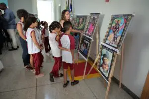 Foto de uma mulher seguida de algumas crianças em frente a quadros de arte.