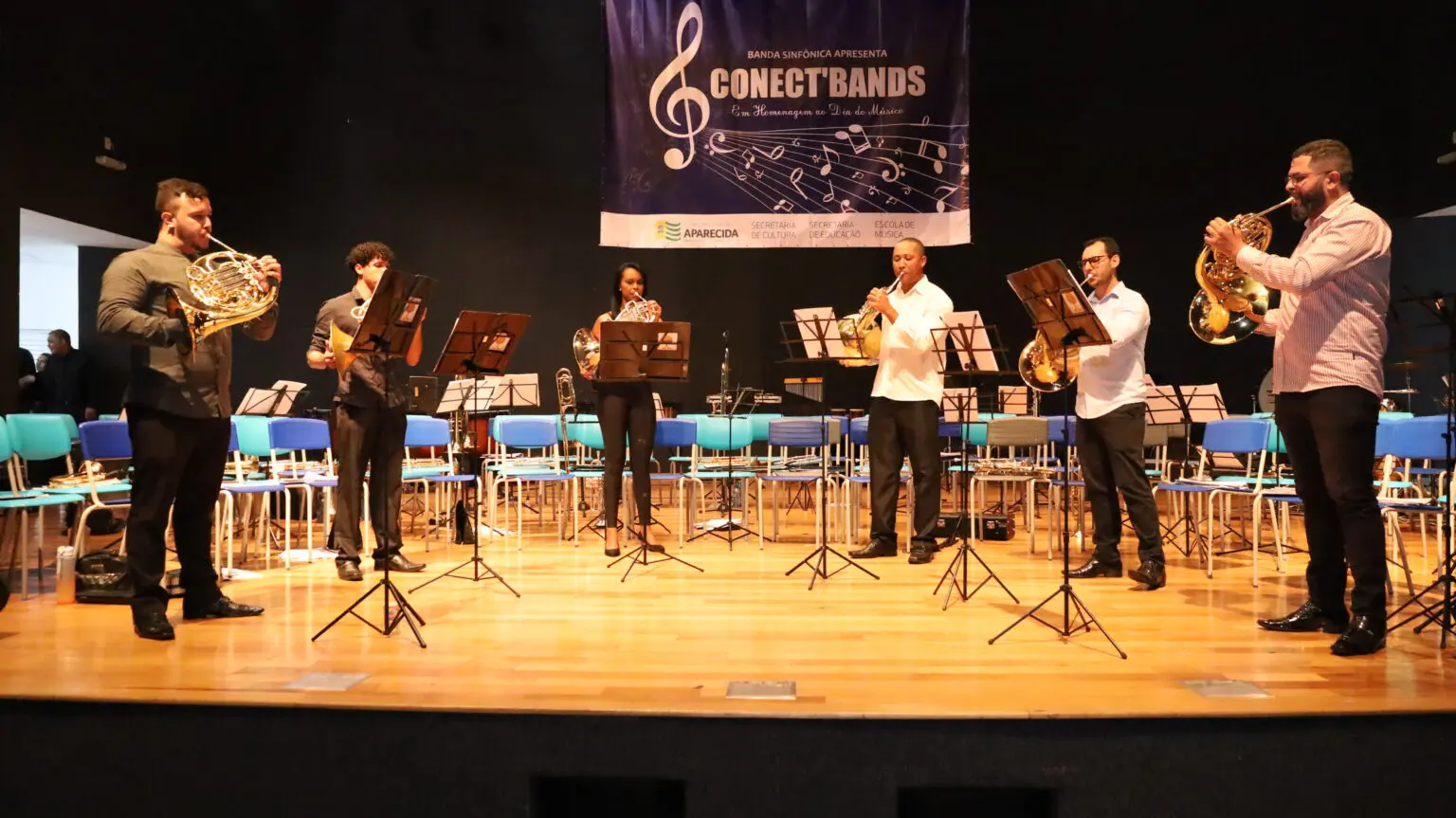 Foto de pessoas tocando instrumentos musicais em um palco.