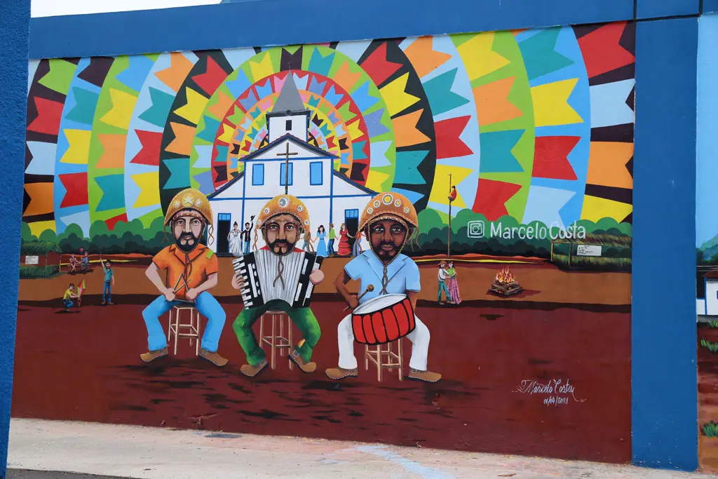 Foto de arte urbana, de 3 pessoas e ao fundo a igreja de aparecida.