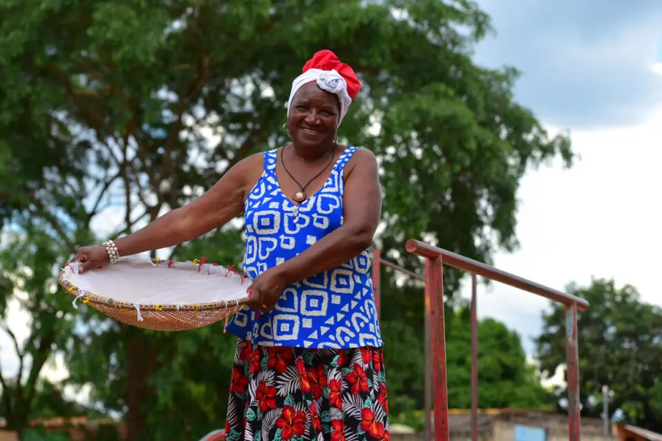 Foto de uma mulher negra, segurando uma peneira.