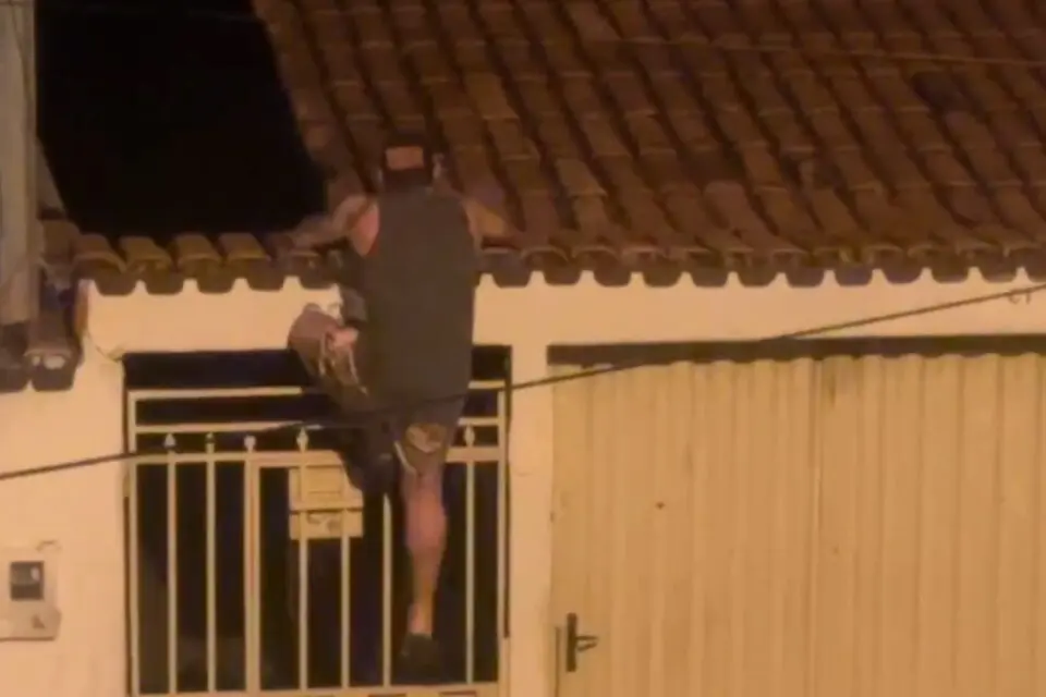 Foto de um homem escalando a parede de uma residência.