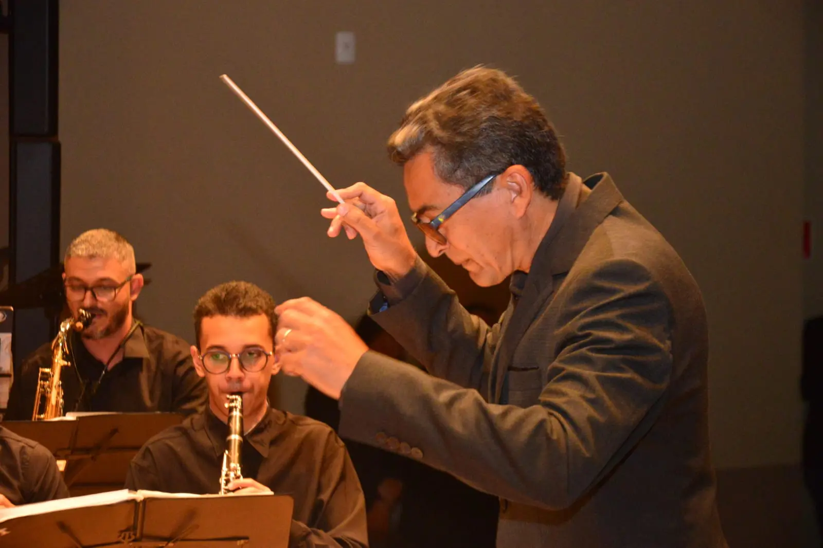 Foto do maestro conduz músicos durante apresentação.