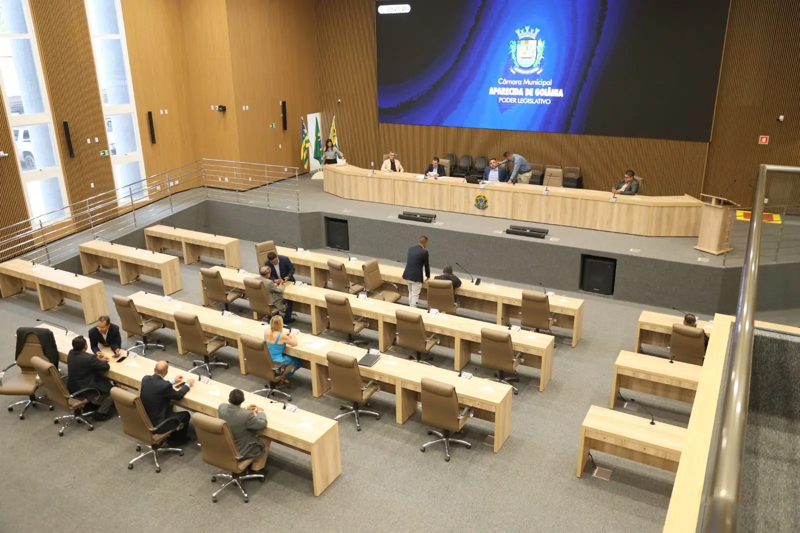 Plenário da Câmara Municipal de Aparecida de Goiânia durante uma sessão, com poucos vereadores presentes. O ambiente destaca o espaço amplo e moderno do legislativo loca