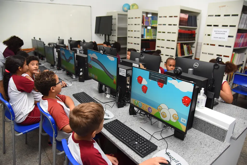 Crianças participam de atividades educacionais em um laboratório de informática, utilizando computadores para aprender de forma interativa e tecnológica em ambiente escolar.