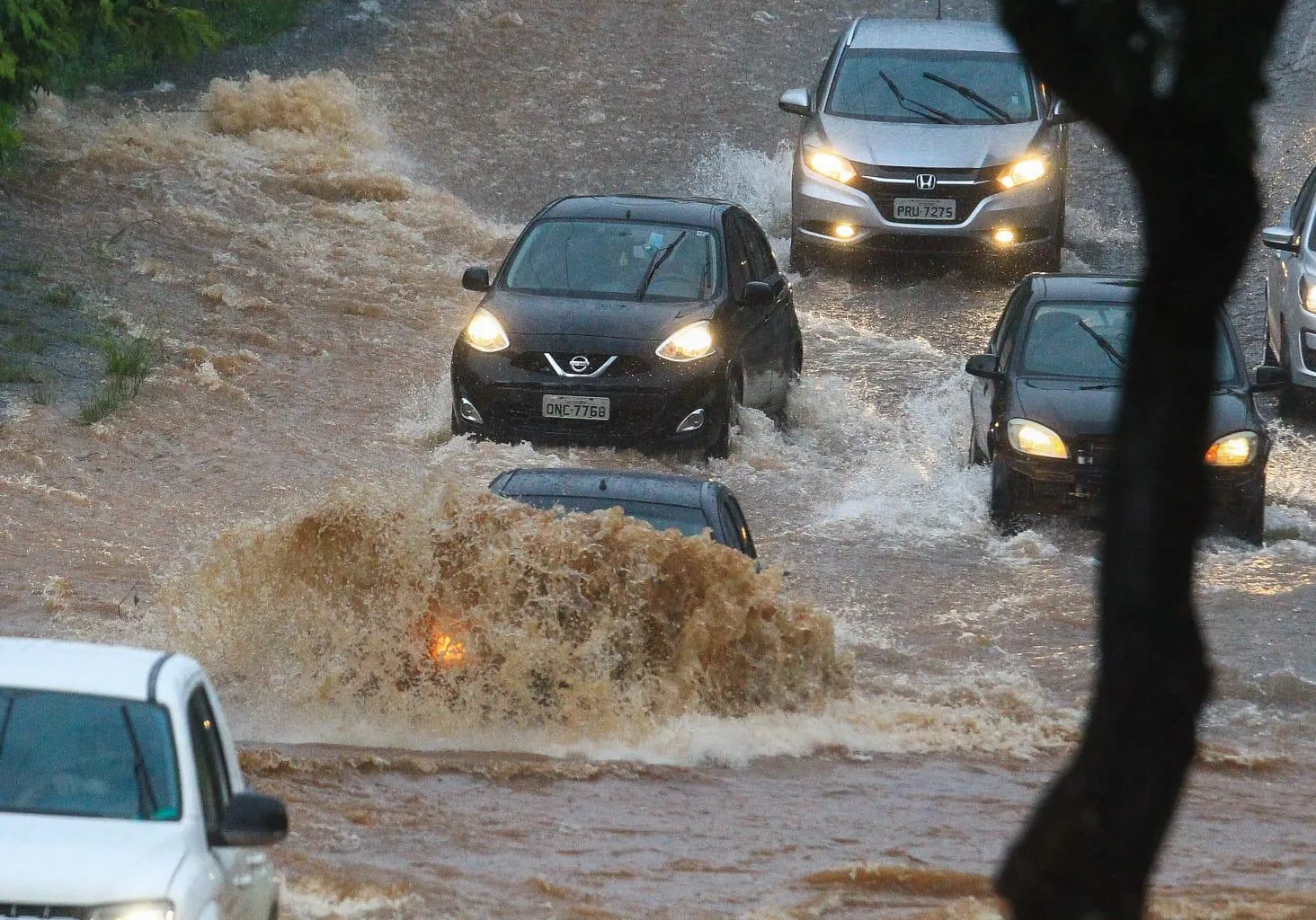 Foto de veículos transitando em via com água acumulada.