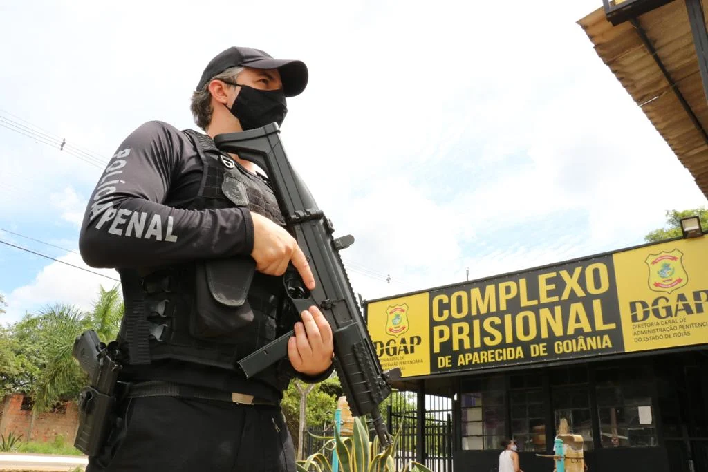 Um agente da Polícia Penal, armado e uniformizado, está em frente ao Complexo Prisional de Aparecida de Goiânia